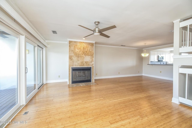 unfurnished living room with ornamental molding, ceiling fan, a tile fireplace, light wood-type flooring, and baseboards