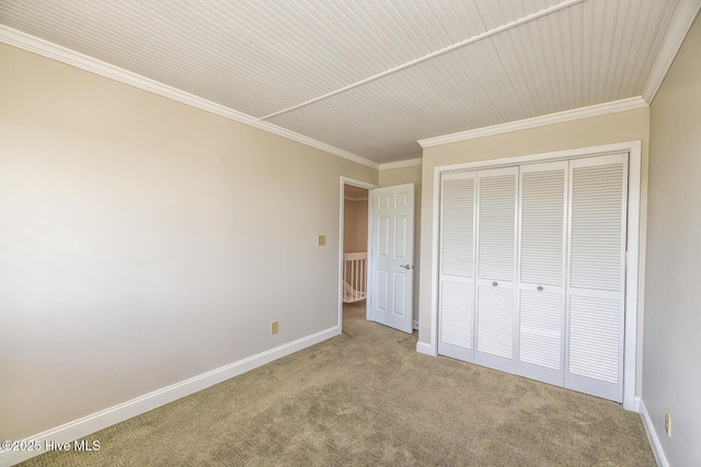 unfurnished bedroom featuring carpet floors, crown molding, baseboards, and a closet