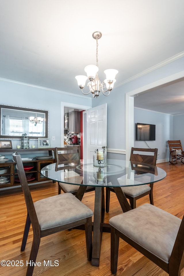 dining area featuring a chandelier, ornamental molding, and light wood finished floors