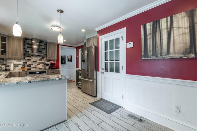 kitchen featuring stainless steel fridge with ice dispenser, wall chimney range hood, oven, ornamental molding, and wainscoting