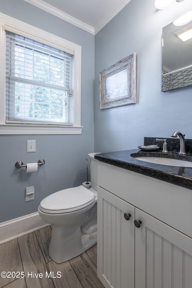 bathroom featuring toilet, wood finished floors, ornamental molding, vanity, and baseboards