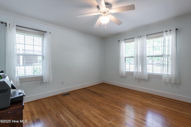 empty room featuring wood finished floors, healthy amount of natural light, crown molding, and baseboards