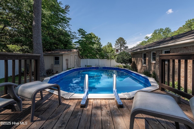 view of pool featuring a deck, an outbuilding, a fenced backyard, and a storage shed