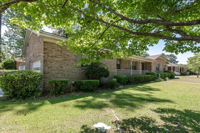 view of side of home featuring brick siding, a lawn, an attached garage, and covered porch