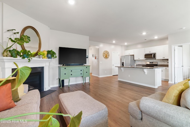 living area featuring wood finished floors, recessed lighting, a fireplace with flush hearth, and baseboards
