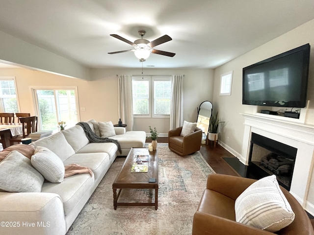 living room featuring a ceiling fan, a fireplace with flush hearth, baseboards, and wood finished floors