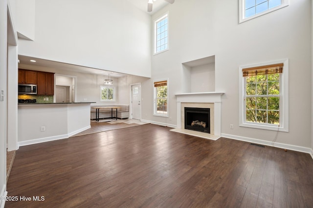 870 Wine Cellar Cir, Wilmington, NC 28411 - unfurnished living room featuring a towering ceiling, dark wood-style floors, a fireplace, ceiling fan, and baseboards
