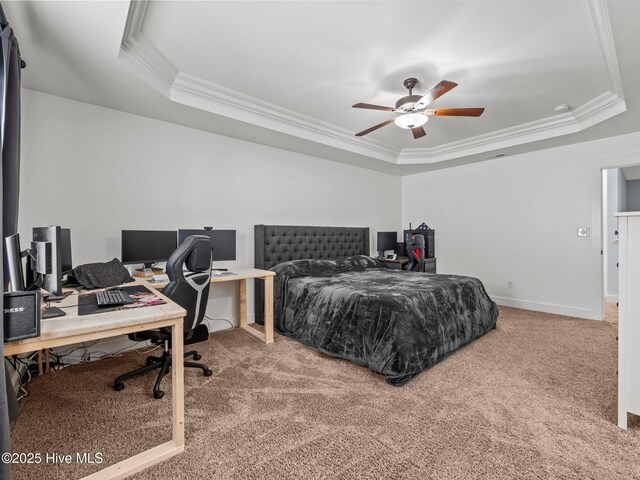 carpeted bedroom featuring a raised ceiling, ornamental molding, a desk, baseboards, and ceiling fan
