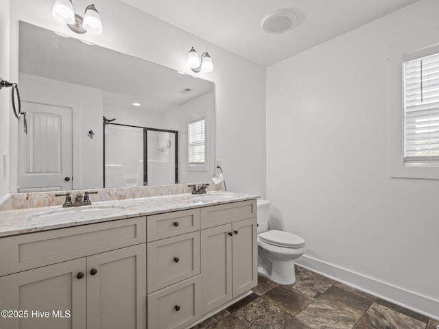 bathroom featuring a stall shower, baseboards, toilet, double vanity, and stone finish flooring
