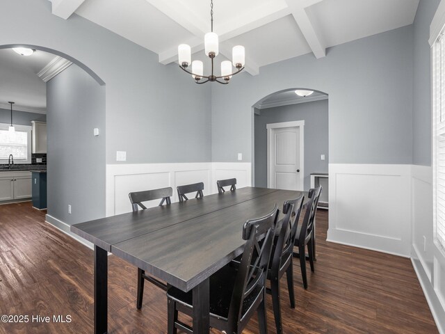 dining room with arched walkways, a wainscoted wall, dark wood finished floors, beamed ceiling, and a chandelier
