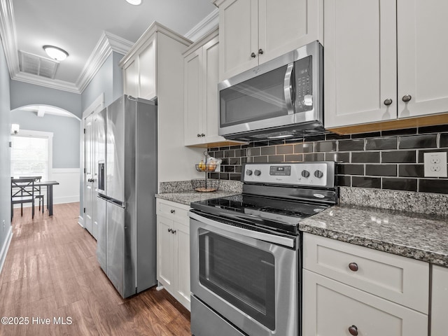 kitchen with stainless steel appliances, arched walkways, crown molding, white cabinets, and dark stone counters
