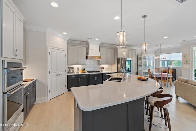 kitchen featuring a sink, custom range hood, stainless steel appliances, ornamental molding, and a kitchen bar