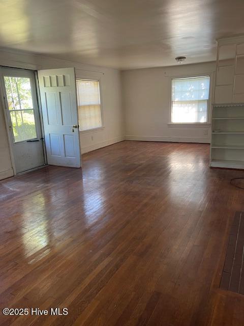 unfurnished living room with dark wood-type flooring and baseboards