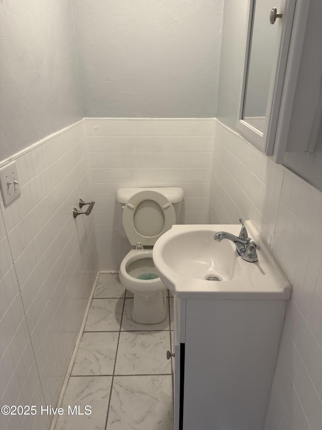 bathroom with marble finish flooring, toilet, vanity, and wainscoting
