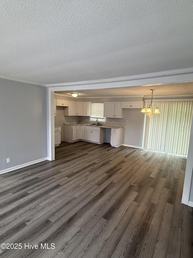 unfurnished living room with a textured ceiling, dark wood-style flooring, a chandelier, ornamental molding, and baseboards