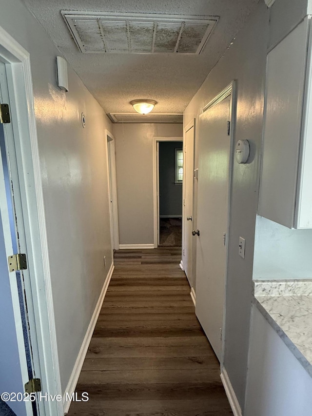 hall with attic access, dark wood finished floors, a textured ceiling, and baseboards