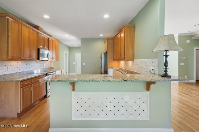 kitchen with appliances with stainless steel finishes, a peninsula, light wood finished floors, a breakfast bar area, and decorative backsplash