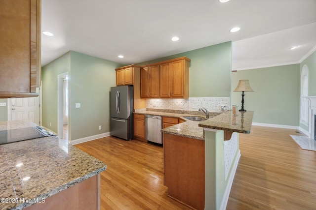 kitchen with appliances with stainless steel finishes, a peninsula, a sink, light wood-style flooring, and baseboards