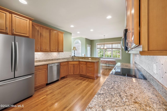 kitchen with appliances with stainless steel finishes, light wood-type flooring, a peninsula, a sink, and tasteful backsplash