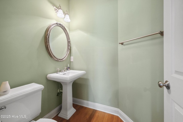 half bath with toilet, wood finished floors, and baseboards