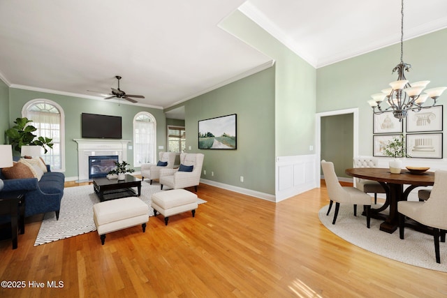 living area with light wood finished floors, ornamental molding, a chandelier, ceiling fan, and a glass covered fireplace