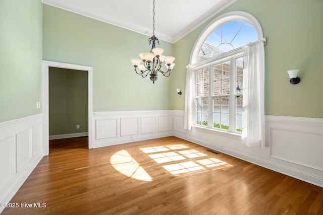 unfurnished dining area featuring a chandelier, wainscoting, ornamental molding, and light wood-style flooring
