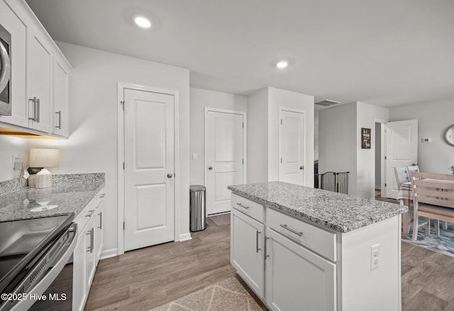 kitchen with a kitchen island, white cabinetry, light wood-type flooring, light stone countertops, and recessed lighting
