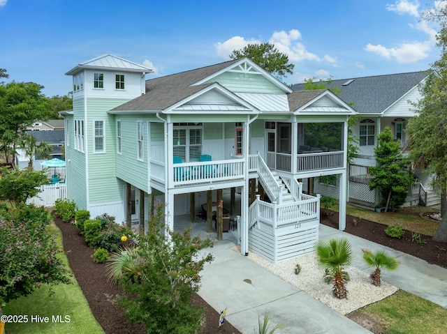 coastal home featuring a standing seam roof, roof with shingles, concrete driveway, and metal roof