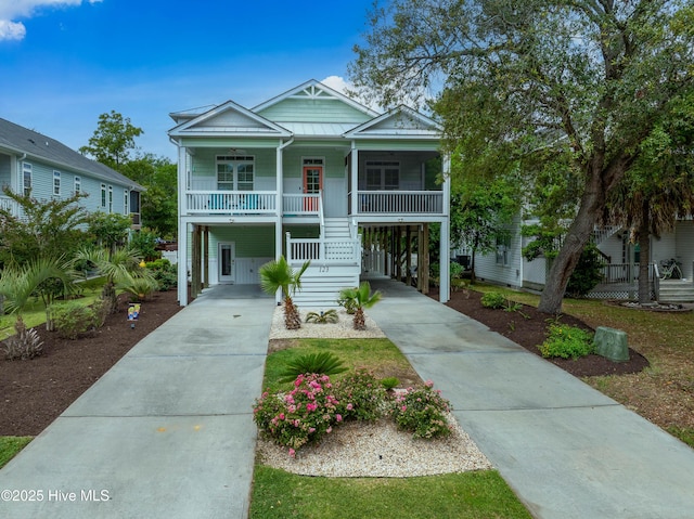 raised beach house with concrete driveway, a porch, a carport, a standing seam roof, and metal roof