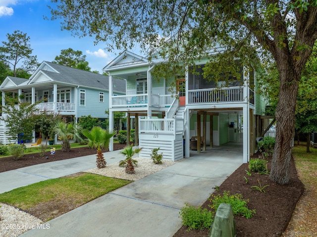 beach home featuring a carport, concrete driveway, a porch, and stairs