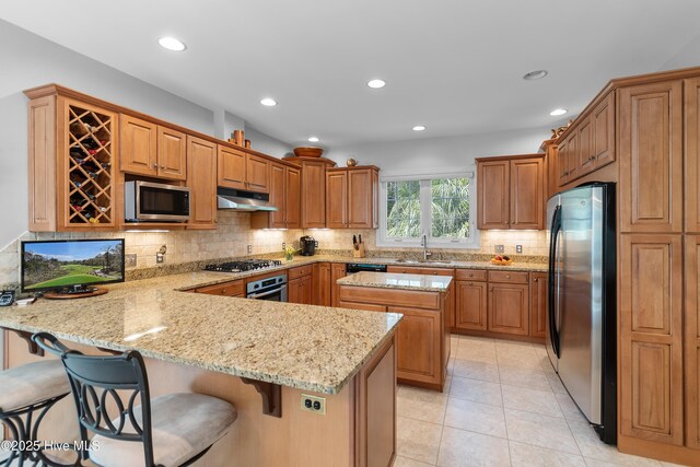 kitchen featuring appliances with stainless steel finishes, a peninsula, under cabinet range hood, light stone countertops, and tasteful backsplash