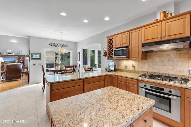 kitchen featuring appliances with stainless steel finishes, under cabinet range hood, a peninsula, tasteful backsplash, and light stone countertops
