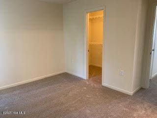 unfurnished bedroom with a walk in closet, carpet, a closet, and baseboards