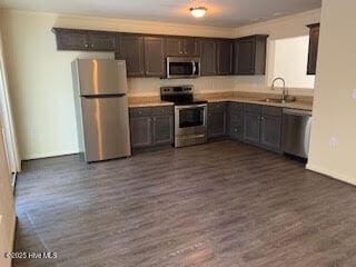 kitchen featuring appliances with stainless steel finishes, a sink, dark wood finished floors, dark brown cabinets, and baseboards
