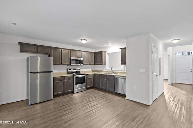 kitchen with stainless steel appliances, a sink, wood finished floors, light countertops, and ornamental molding