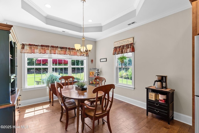 dining room featuring healthy amount of natural light, hardwood / wood-style floors, a chandelier, ornamental molding, and a raised ceiling