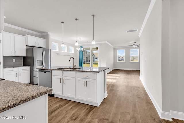 kitchen with a sink, stainless steel appliances, dark stone counters, light wood-style flooring, and ceiling fan