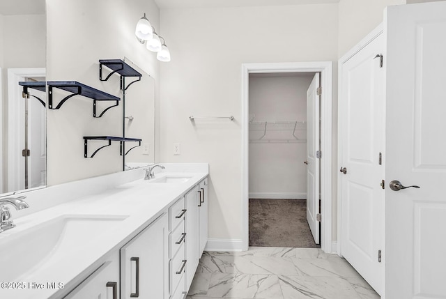 bathroom with marble finish floors, double vanity, a walk in closet, and baseboards