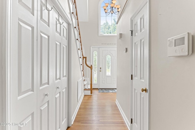 foyer entrance with a chandelier, baseboards, light wood finished floors, and a high ceiling