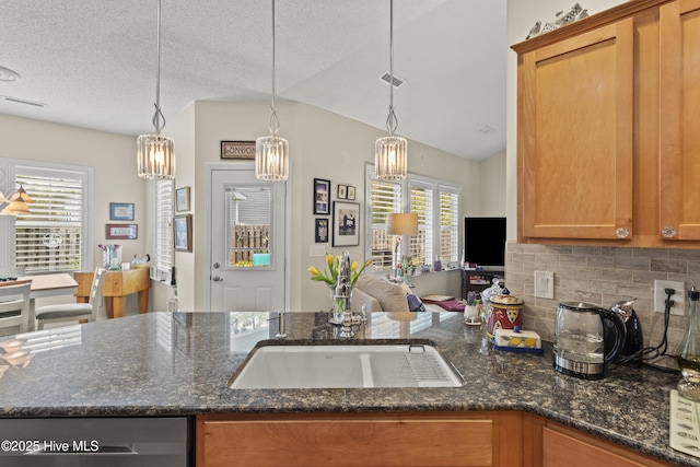 kitchen featuring tasteful backsplash, brown cabinetry, lofted ceiling, plenty of natural light, and a sink