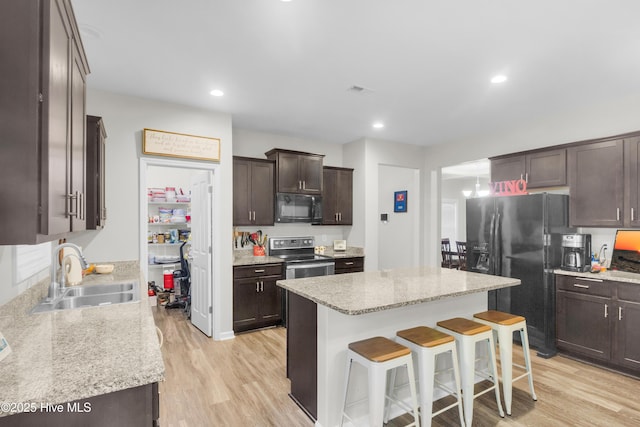 kitchen with black appliances, a sink, dark brown cabinetry, a kitchen breakfast bar, and a center island