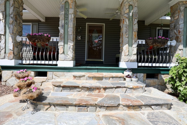 doorway to property featuring a porch, a ceiling fan, and stone siding
