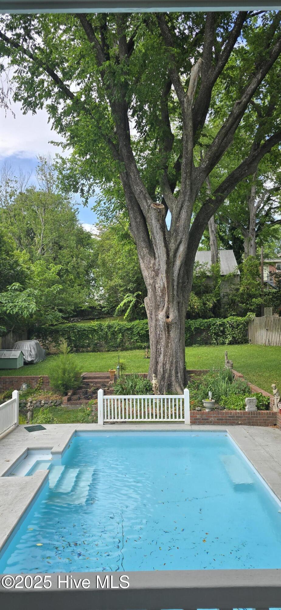 view of swimming pool featuring a hot tub, fence, and view of wooded area