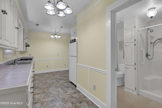211 Ann St, Wilmington, NC 28401 - kitchen with a chandelier, freestanding refrigerator, a sink, white cabinetry, and under cabinet range hood