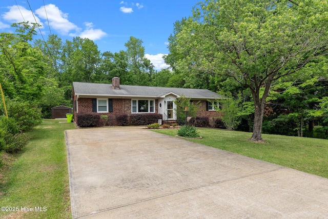 ranch-style house with driveway, a chimney, a front yard, brick siding, and a shed