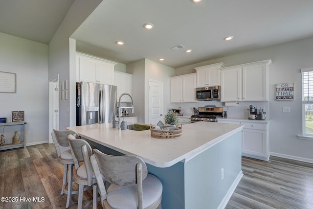6909 English Holly Ct SW, Ocean Isle Beach, NC 28469 - kitchen featuring appliances with stainless steel finishes, wood finished floors, a large island with sink, white cabinetry, and baseboards