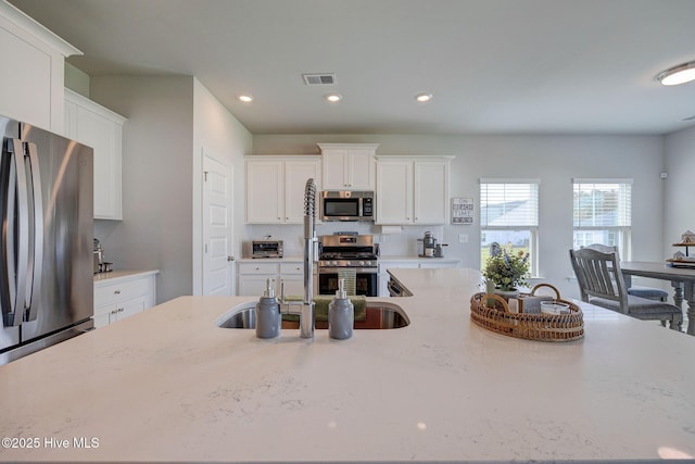 6909 English Holly Ct SW, Ocean Isle Beach, NC 28469 - kitchen with appliances with stainless steel finishes, white cabinetry, a sink, recessed lighting, and light stone counters