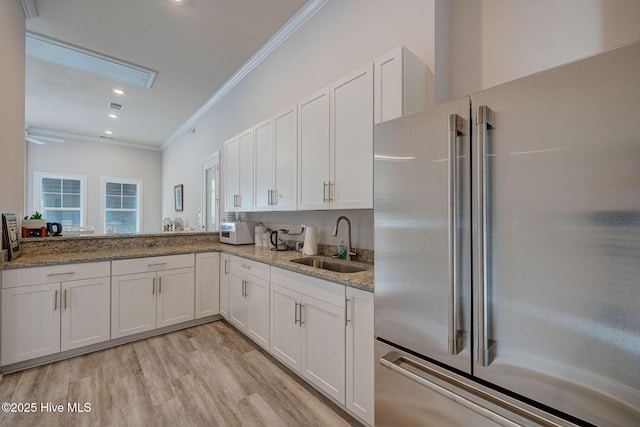 6909 English Holly Ct SW, Ocean Isle Beach, NC 28469 - kitchen with high quality fridge, a sink, crown molding, white cabinetry, and light stone counters