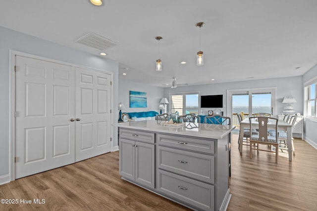 kitchen featuring gray cabinets, open floor plan, light countertops, wood finished floors, and decorative light fixtures