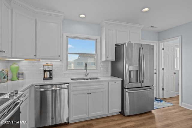 kitchen with appliances with stainless steel finishes, a sink, white cabinets, light countertops, and recessed lighting